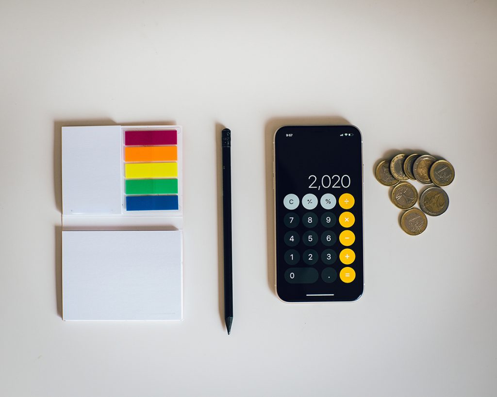 A pen and sticky notes with a phone calculating an amount of money
