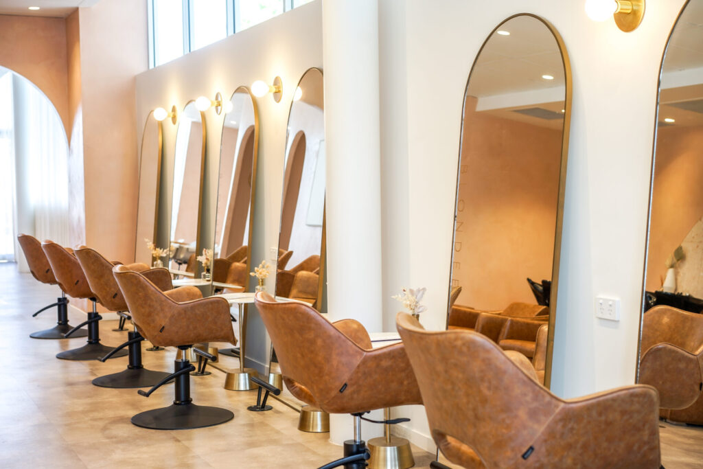 Rounded gold mirrors, neutral and brown colour palette and welcoming reception area for this wellness & beauty fit out for Blondee Salon