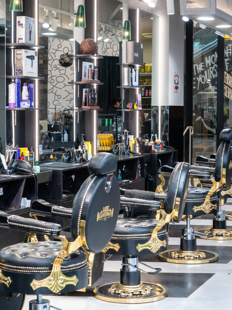 Gold and black barber chairs, checkered black and white floor pattern and motorbike ceiling feature for this wellness & beauty fit out for Gabriel Barber