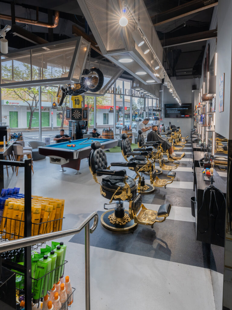 Gold and black barber chairs, checkered black and white floor pattern and motorbike ceiling feature for this wellness & beauty fit out for Gabriel Barber
