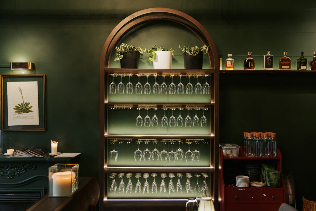 Curved bespoke timber glasses holder, deep green and brown colour palette and welcoming dining area for this hospitality fit out for Thai Room