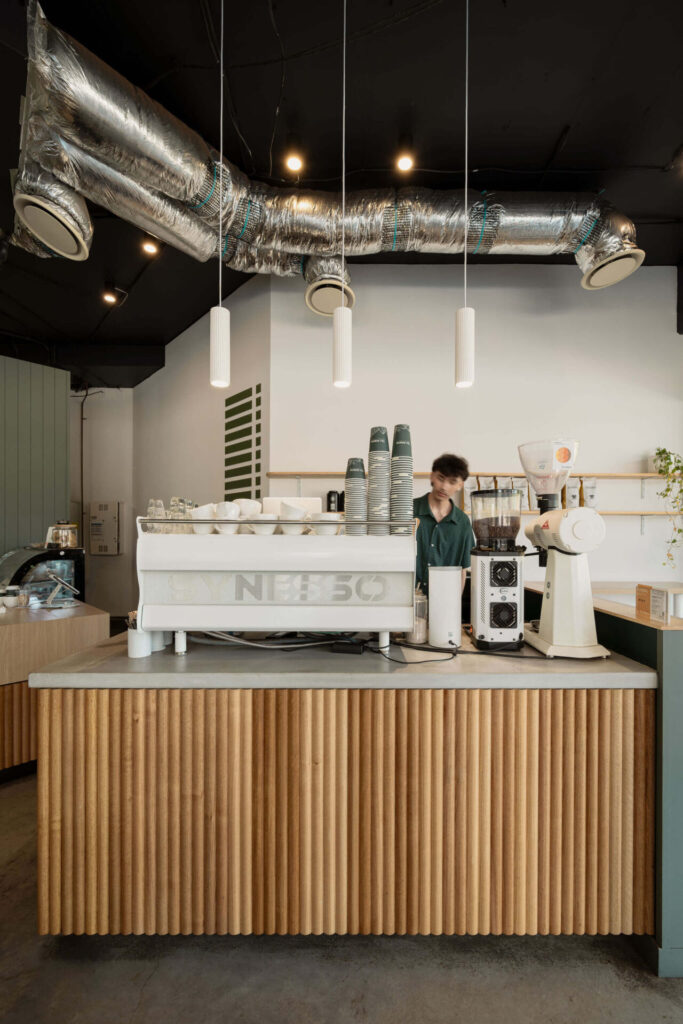 Exposed black high ceiling, bespoke cylinder timber panelled service counter and neutral and green branded colour palette for this hospitality fit out for Tim Adams Cafe, Total Fitouts Sunshine Coast South